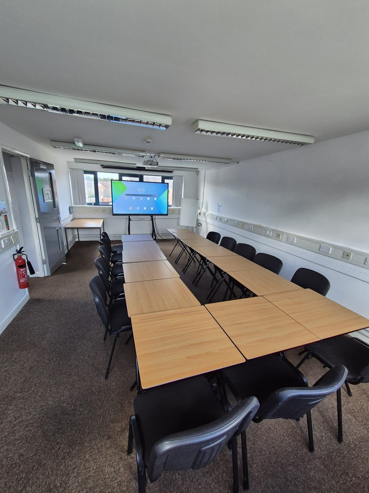 The training room at Platt Bridge Community Zone, set out with tables and chairs in a U-shape facing a large touchscreen display