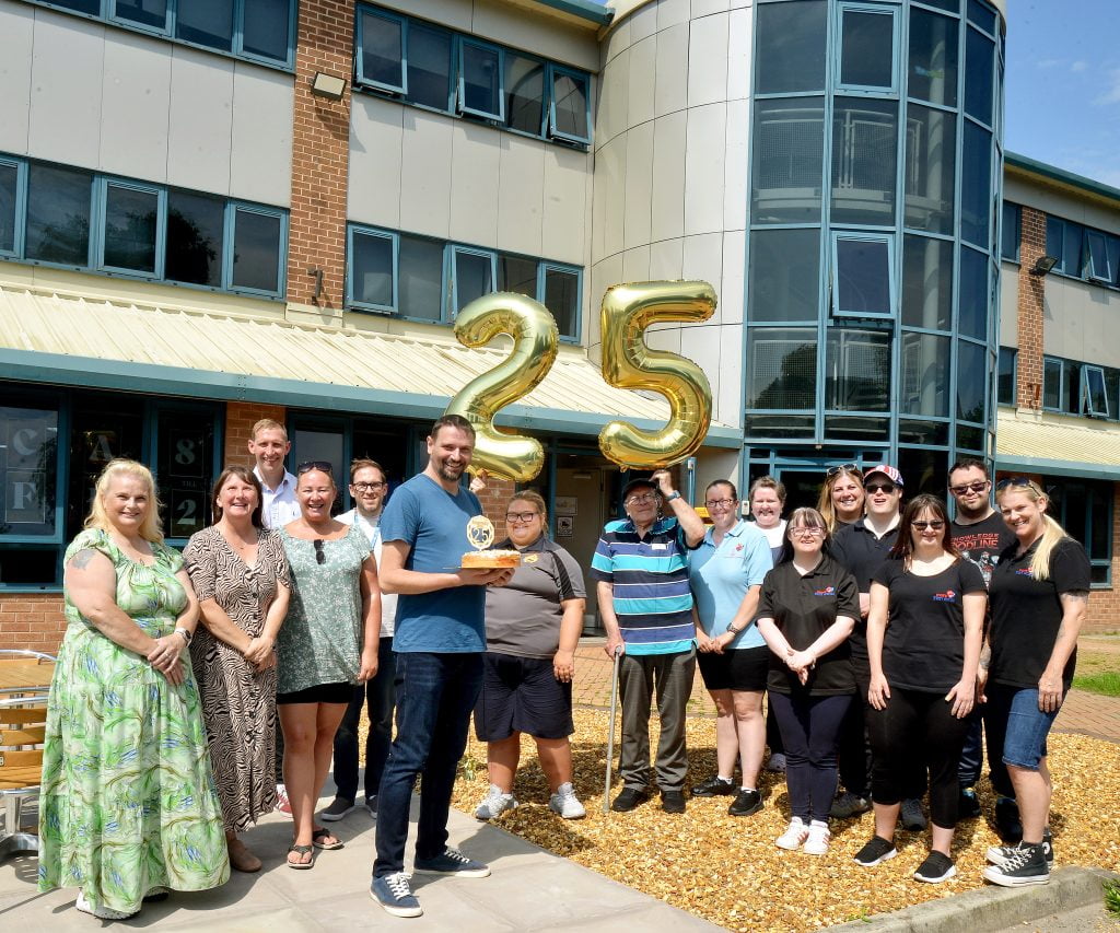 Wigan & Leigh Community Charity staff and volunteers gathered outside their offices with gold '25' balloons to mark 25 years