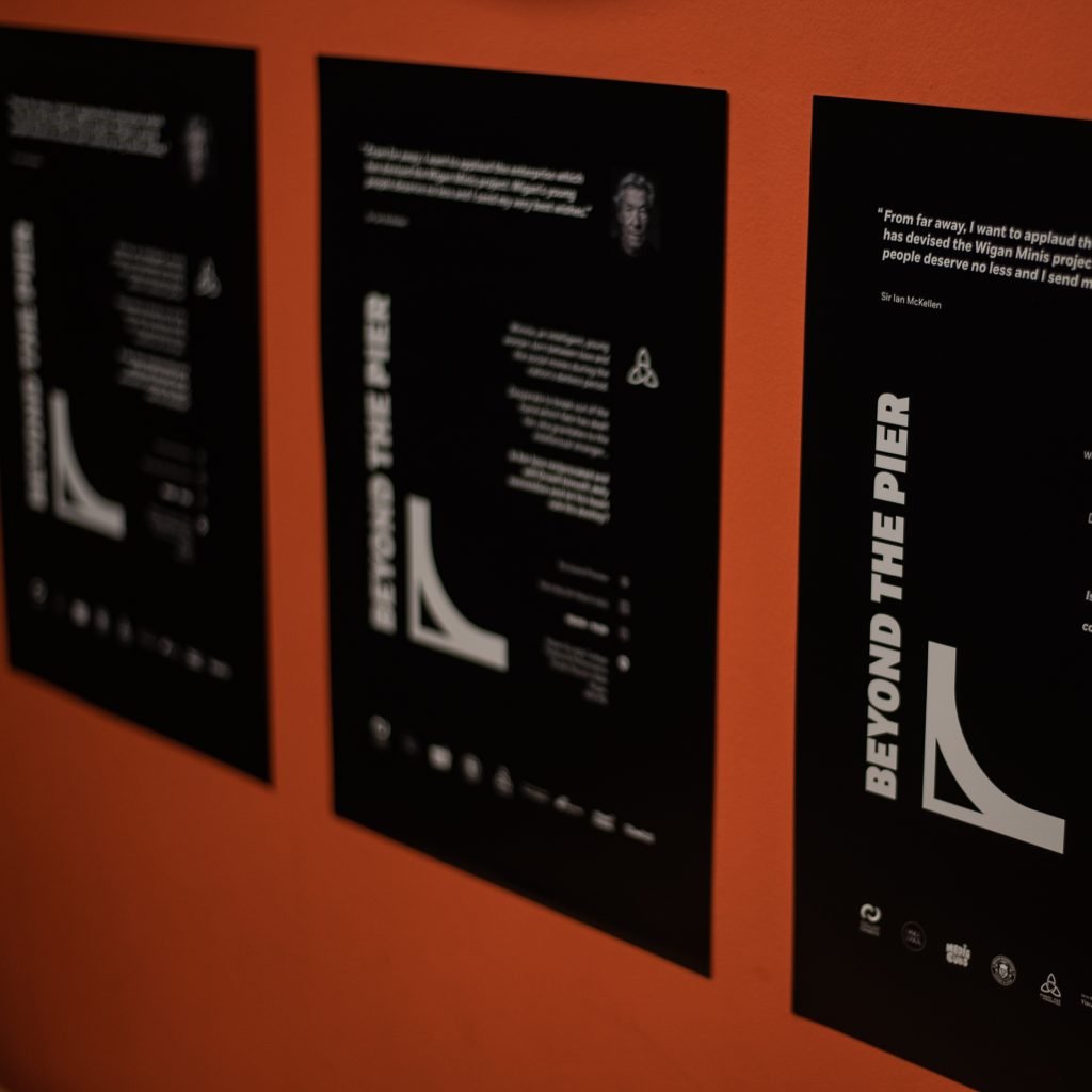 Beyond the Pier exhibition boards mounted on an orange wall, including a quote of support from Sir Ian McKellen