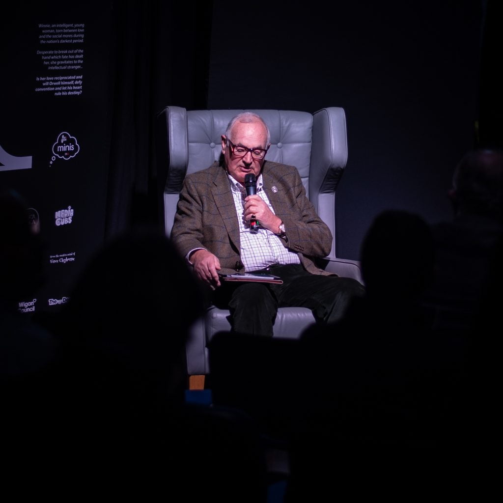 A speaker addressing the audience from an armchair on stage at the Beyond the Pier preview show