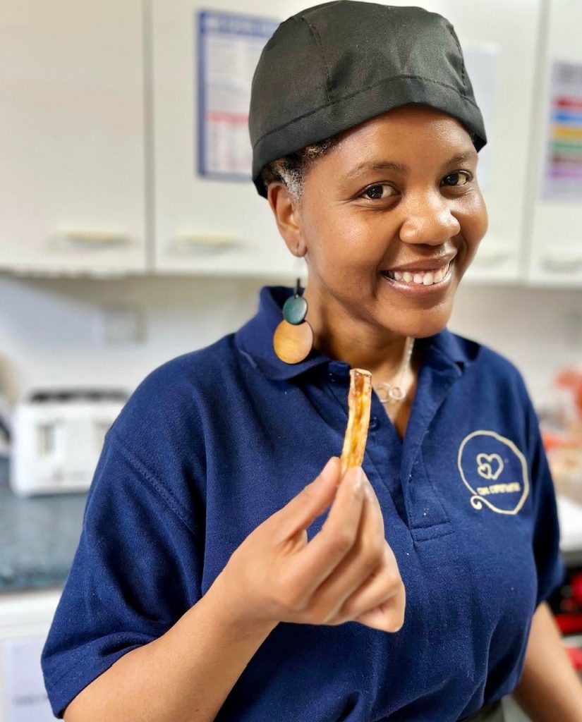 A smiling Café Camaraderie team member holding a slice of toast in the café kitchen