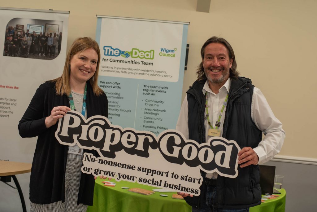 Two people holding a large Proper Good sign reading 'No-nonsense support to start or grow your social business'
