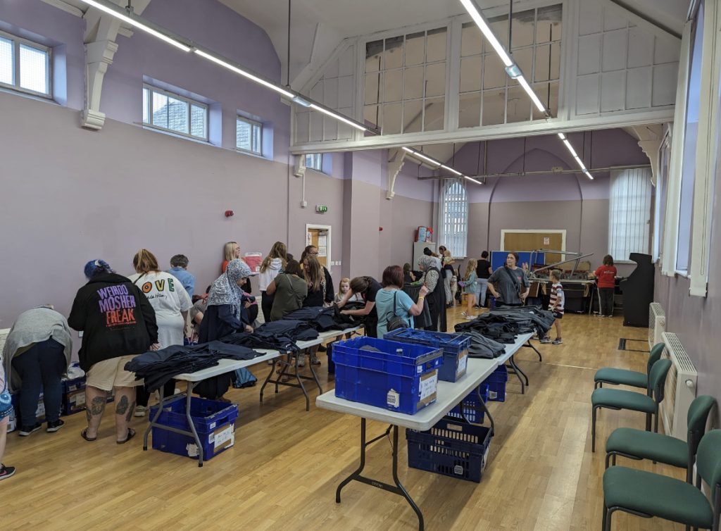 Volunteers sorting donated clothing into crates on trestle tables in a community hall