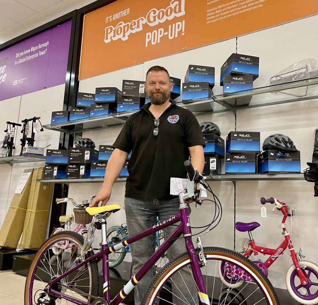 A volunteer with a refurbished Raleigh bicycle at the Proper Good pop-up, cycle helmets stocked on the shelves behind