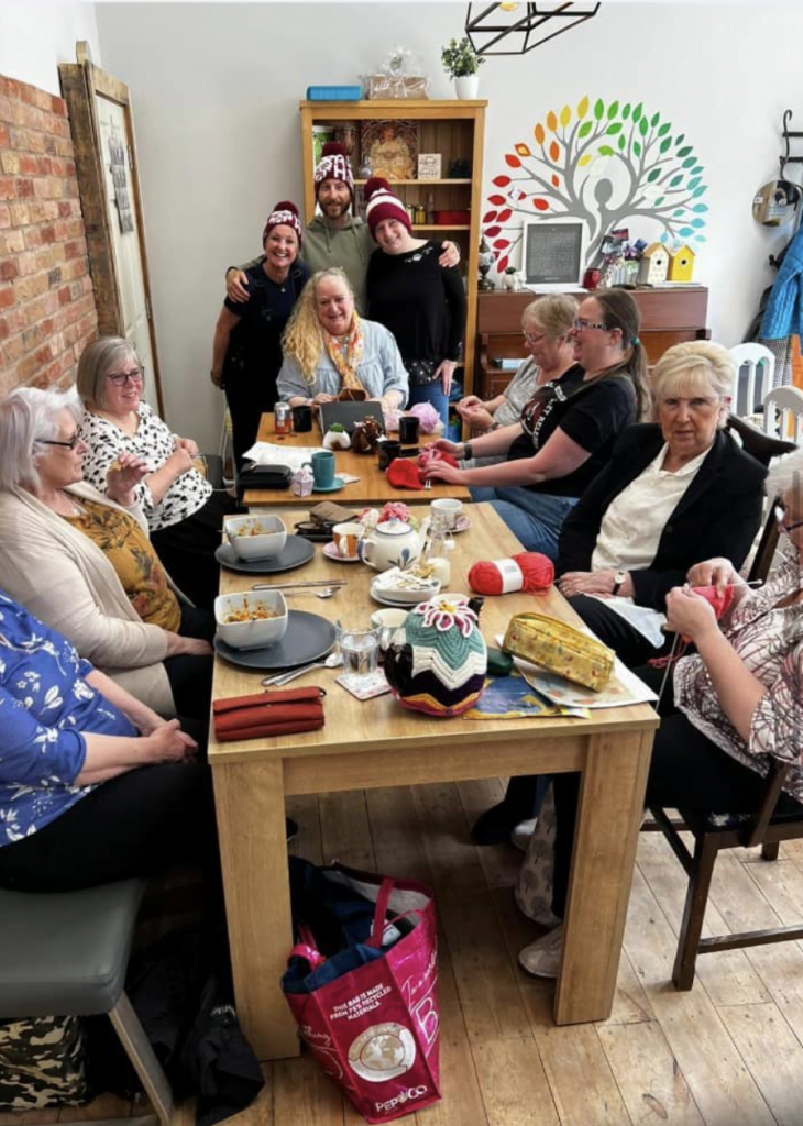 Members of a craft and knitting group sitting around a long table in a community room