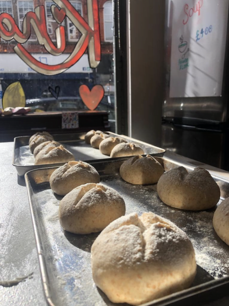 A tray of freshly shaped bread rolls dusted with flour in the café kitchen
