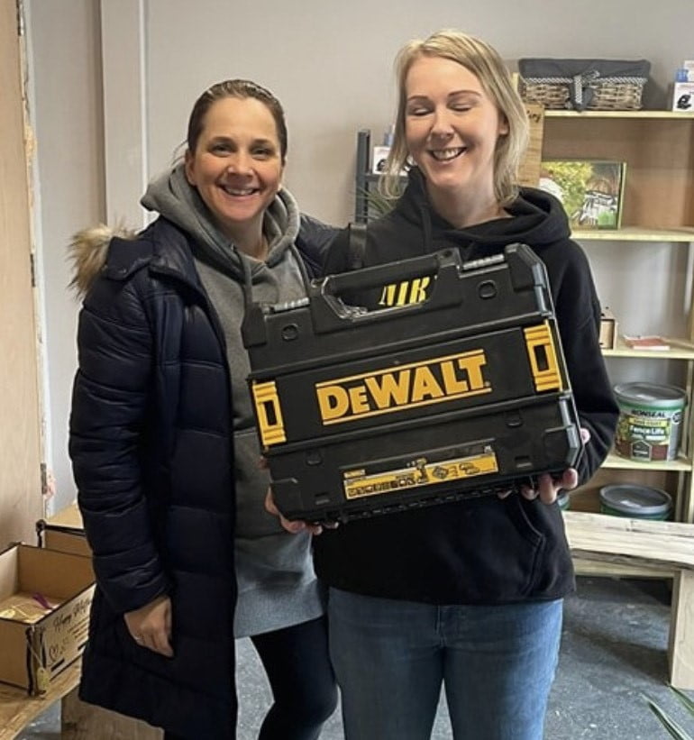 Two participants holding a donated DeWalt tool case in the community workshop